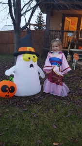 Photo of Hailey dressed as Mulan for Halloween standing outside smiling beside an inflatable ghost. 